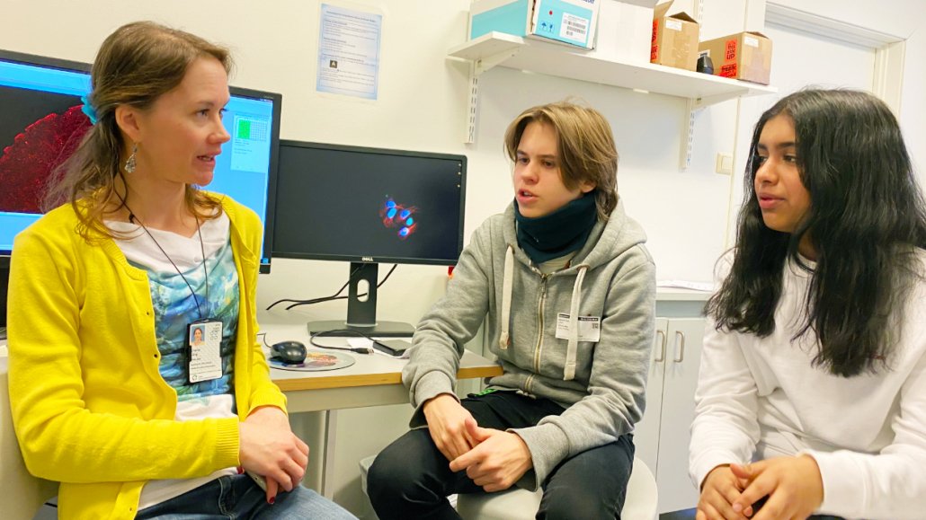 Emma Lång is a researcher at the research group Experimental Cancer Therapy. She explains to Henrik and Isha how the advanced microscope, connected to the computer behind her, can record videos of living cells. Photo: Elisabeth Kirkeng Andersen