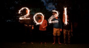 The number 2021 in sparkling light held by four persons we can hardly see