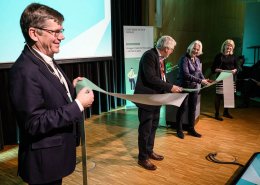 Four people on a stage cutting a ribbon