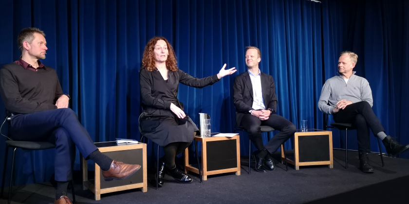 Three people in a discussion on a stage, sitting, one of which is Camilla Stoltenberg, who is engaged with her arm in a gesture.